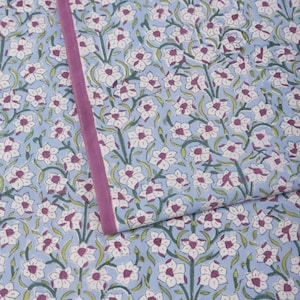 May include: A light blue floral patterned fabric with white flowers, purple centers, and green leaves. A vertical purple border runs along the edge of the fabric. The fabric is likely used for bedding or home decor.
