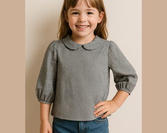 May include: A girl's black and white gingham blouse with a rounded collar and three-quarter sleeves. The girl is also wearing denim shorts. The girl is smiling and has her hand on her hip.
