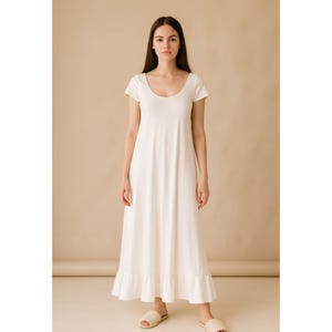 May include: A white, scoop-neck maxi dress with short sleeves and a ruffled hem. The dress is made of a soft, flowing fabric and is suitable for casual wear. The model is wearing beige sandals.