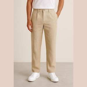 May include: Beige linen trousers with a pleated front. The trousers are worn with a white t-shirt and white trainers. The trousers have a relaxed fit and a button and zip closure.