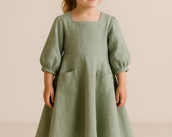 Puede incluir: Un vestido verde claro con cuello cuadrado y mangas cortas abullonadas. El vestido tiene dos bolsillos delanteros y una falda acampanada. La tela parece ser lino o un material ligero similar, adecuado para niños.