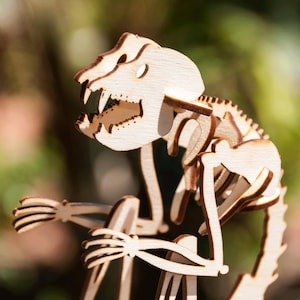 May include: A wooden model of a skeleton of a small animal, possibly a monkey, with a long tail. The model is made of light brown wood and is posed in a sitting position.