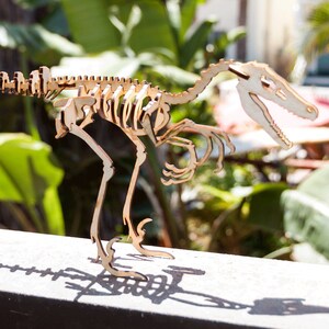 May include: A wooden model of a dinosaur skeleton, with a long tail and a large head. The model is made of light brown wood and is standing on a dark surface.