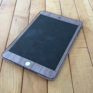 May include: A tablet with a wood grain effect case, placed on a light brown wooden surface. The tablet's screen is black, and the case has a natural wood appearance. The tablet is angled, showing its side and front.