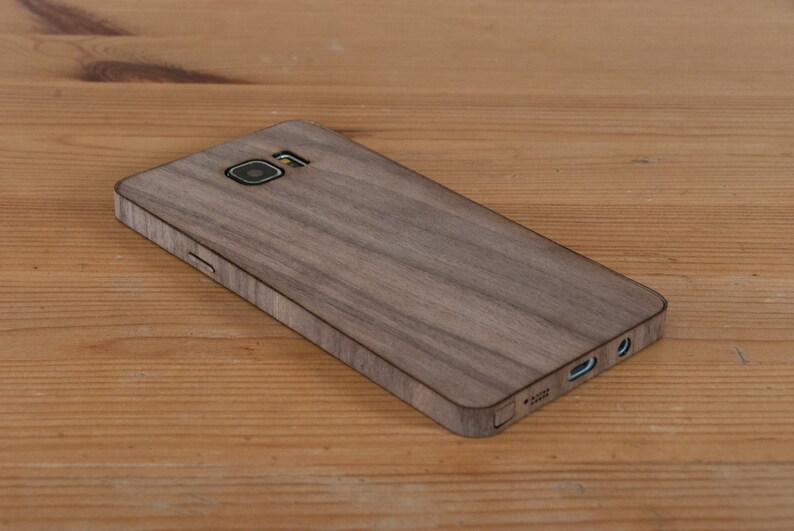 May include: A brown wood phone case with a textured wood grain pattern. The case has a camera cutout and a cutout for the charging port.