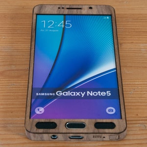 May include: A wooden phone case for a Samsung Galaxy Note 5. The case is made of dark wood and has a natural wood grain. The phone screen shows the time as 12:45 and the date as Fri, 21 August.