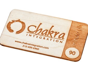 Op de afbeelding: Een houten cadeaubon voor 90 minuten chakra-integratie. De cadeaubon heeft een cirkel met een lijn erdoorheen, de woorden "chakra integration", een website-adres en een telefoonnummer. De cadeaubon is bruin en heeft een lichtbruine rand.
