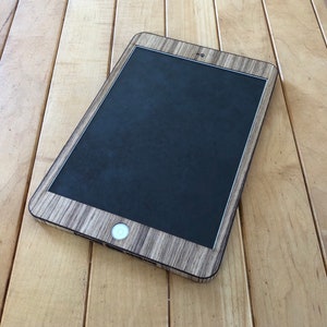 May include: A black tablet computer with a wood-grain patterned case. The tablet is lying on a wooden surface.