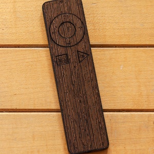 Puede incluir: Un mando a distancia de madera con un botón circular, un botón de reproducción, un botón de pausa y un botón de avance rápido.