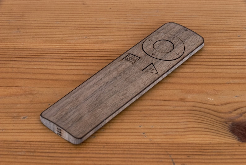May include: A wooden remote control with etched symbols and a circular navigation pad. The remote is rectangular with rounded edges and a wood grain finish. It rests on a wooden surface.