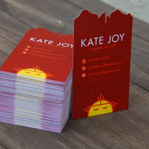 May include: A stack of red business cards with a stylized sun design and the text "Kate Joy, Proprietor, Sun Cliff" and contact information.