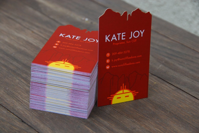 May include: A stack of red business cards with a stylized sun design and the text "Kate Joy, Proprietor, Sun Cliff" and contact information.