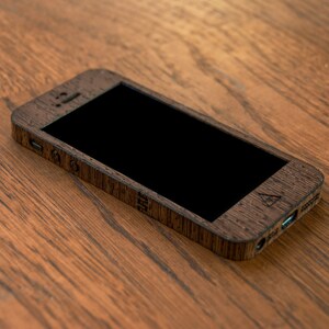 May include: A wooden phone case with a black screen. The case has a dark brown wood grain pattern and a small logo on the back.