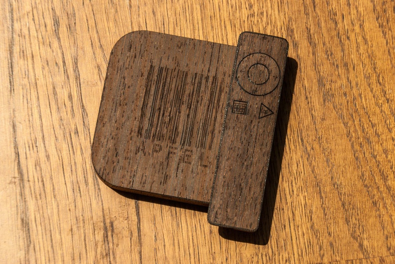 May include: A dark brown wooden device with a rectangular section and a rounded section. The rectangular section has a barcode and the word "APFEL" etched into it. The rounded section has control symbols etched into it.