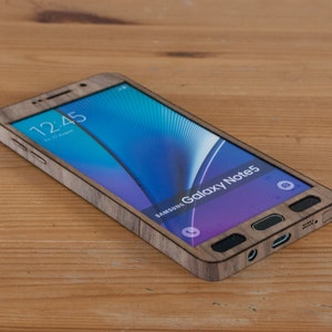 May include: A Samsung Galaxy Note 5 smartphone with a wooden case. The phone is on a wooden surface and the screen shows the time 12:45.