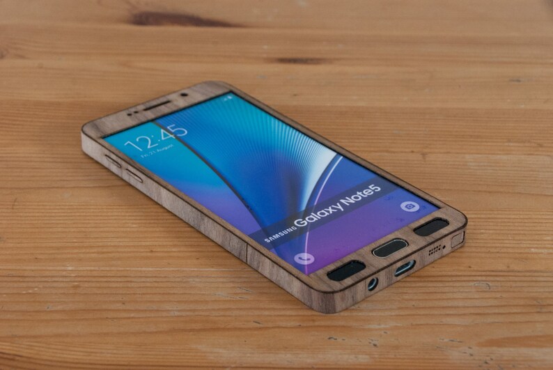 May include: A Samsung Galaxy Note 5 smartphone with a wooden case. The phone is on a wooden surface and the screen shows the time 12:45.