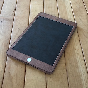 May include: A black tablet computer with a wood grain case. The tablet is lying on a wooden surface.