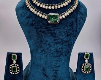 May include: A two-tiered emerald green and white diamond necklace with matching earrings. The necklace features a large emerald green stone in the center.