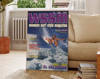 Może przedstawiać: Oprawiona okładka magazynu WSSM, Women's Surf Style Magazine, z surferką na fali. Okładka ma fioletowo-białe logo i napis "EL SALVADOR". Magazyn jest wystawiony na dywanie w pobliżu okna.