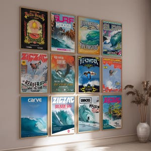 May include: A display of framed surf posters with bright colours and vintage designs. The posters feature surfing scenes, text like "Bells Beach," "Mexico," and "Zigzag," and are displayed on a neutral wall, creating a coastal theme.