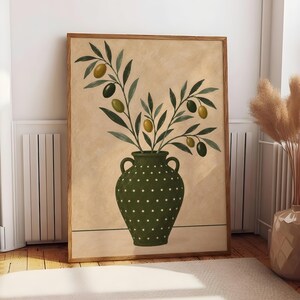 Könnte beinhalten: Ein gerahmter Kunstdruck, der eine dunkelgrüne Vase mit weißen Punkten zeigt. Die Vase enthält mehrere Olivenzweige mit grünen und dunkelbraunen Oliven sowie langen, spitzen Blättern. Der Hintergrund ist einfarbig hellbeige mit einer dünnen horizontalen Linie am unteren Rand, eingefasst in einen schlichten Holzrahmen.