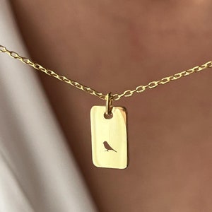 May include: A gold chain necklace with a small rectangular pendant featuring a cut-out silhouette of a bird.