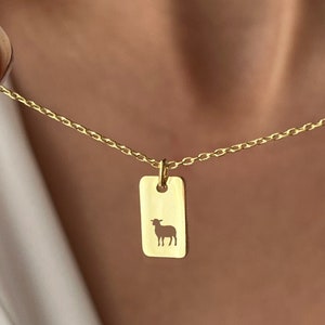 May include: A gold chain necklace with a rectangular pendant featuring a cutout silhouette of a sheep.