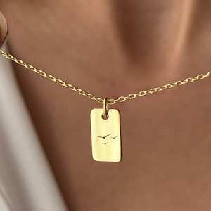 以下が含まれることがあります： 2羽の鳥が飛んでいる繊細なデザインが施された長方形のペンダントが付いたゴールドチェーンネックレスです。