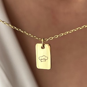 May include: Gold chain necklace with a rectangular pendant featuring a chef hat design.