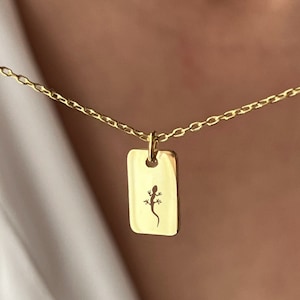 Peut inclure: Un collier en chaîne dorée avec un pendentif rectangulaire orné d'une découpe délicate d'un lézard.