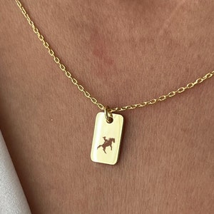 Pode incluir: Um colar de corrente de ouro com um pequeno pingente retangular com a silhueta de uma pessoa a cavalo.