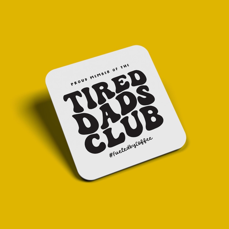 Puede incluir: Posavasos cuadrado blanco con esquinas redondeadas, con el texto "PROUD MEMBER OF THE TIRED DADS CLUB" en negro, en negrita, con fuente retro. La frase "#fueledbycoffee" est&aacute; en la parte inferior. El posavasos est&aacute; sobre un fondo amarillo.
