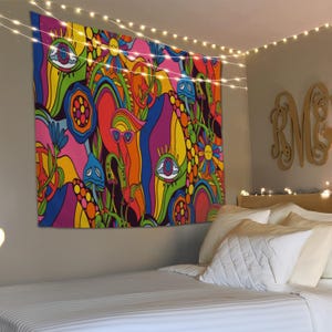 Puede incluir: Un vibrante tapiz psicodélico con un diseño abstracto y colorido que presenta ojos, setas y flores. El tapiz es predominantemente rosa, naranja, amarillo, azul y verde. Cuelga de una pared sobre una cama con ropa de cama blanca, iluminado por luces de cadena.