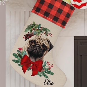 May include: A Christmas stocking with a pug illustration, red bow, and the name "Ellie." The stocking has a red and black buffalo plaid cuff and is decorated with greenery and berries. A red and white swirled lollipop is attached.