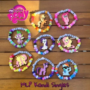 May include: Nine colorful beaded bracelets with My Little Pony characters and names. The bracelets are arranged in three rows on a wooden surface. The text "MLP Kandi Singles" is written below the bracelets.