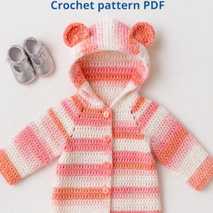 Könnte beinhalten: Gehäkelter Bären-Hoodie in Rosa, Pfirsich und Weiß mit Bärenohren an der Kapuze. Die Jacke mit Knopfleiste wird mit silbernen Babyschuhen präsentiert. Der Text "Bear Crochet Hoodie" und "Crochet pattern PDF" ist im Bild zu sehen.