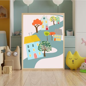 Könnte beinhalten: Ein gerahmter Kunstdruck mit einer skurrilen Illustration von bunten Häusern entlang einer kurvenreichen Straße. Die Häuser haben blaue, gelbe und grüne Dächer, mit Bäumen und einem hellrosa Hintergrund. Das Kunstwerk wird auf einem Holzboden ausgestellt.