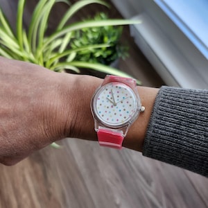 May include: A clear plastic watch with a pink band and a white face with colorful polka dots.