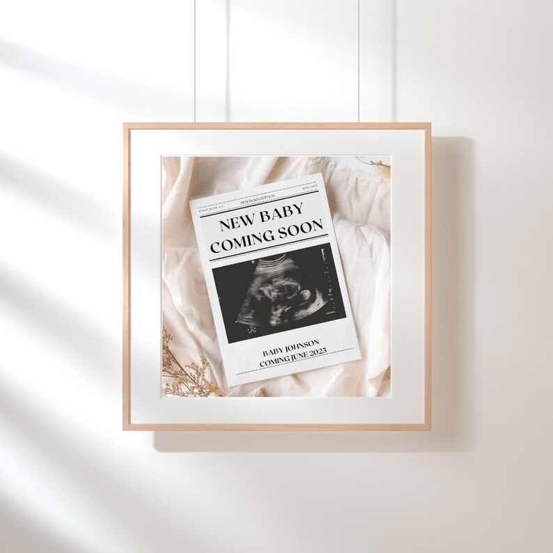 以下が含まれることがあります： 「New Baby Coming Soon」というテキストと超音波画像が書かれた白黒の新聞の発表を額装したもの。画像の下のテキストには「Baby Johnson Coming June 2023」と書いてあります。