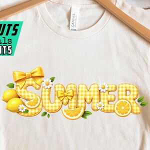 May include: Cream-colored t-shirt with the word "SUMMER" in yellow gingham letters, decorated with lemons, bows, and daisies. The shirt is displayed on a wooden hanger. The text "ARTCUTS DIGITALS & PRINTS" is in the upper left corner.
