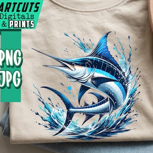 Puede incluir: Camiseta beige con una ilustración de marlín azul y blanco y salpicaduras de agua. La camiseta está doblada sobre unos vaqueros azules. Un sombrero color canela es visible en el fondo. El texto "ARTCUTS DIGITALS & PRINTS" y "PNG JPG" están a la izquierda.