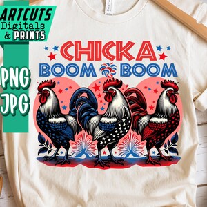 May include: Cream-colored t-shirt featuring a graphic of three roosters in red, white, and blue, with the text "CHICKA BOOM BOOM". The roosters have patriotic designs, and the shirt is displayed on a wooden hanger.