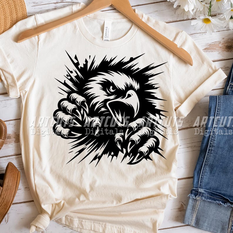 Pode incluir: Uma camiseta branca com um gr&aacute;fico preto de uma &aacute;guia rompendo uma parede. A cabe&ccedil;a e as garras da &aacute;guia s&atilde;o vis&iacute;veis.