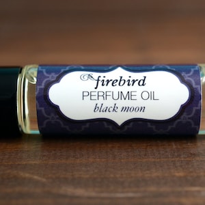 May include: A small glass bottle of perfume oil with a purple and white label. The label says "firebird PERFUME OIL black moon".