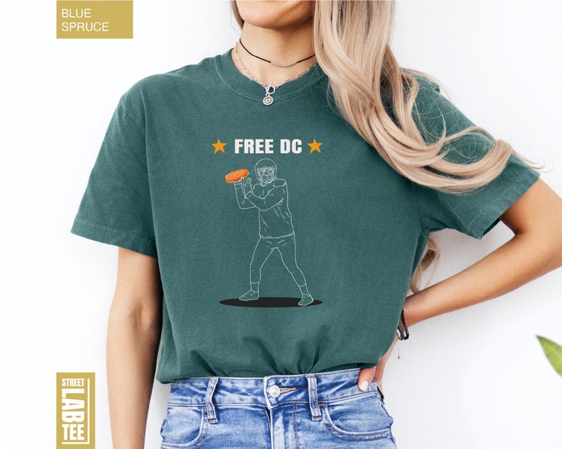 Op de afbeelding: Tealkleurig T-shirt met de tekst "FREE DC" en een afbeelding van een American footballspeler die een bal gooit. Het shirt is een Street Lab Tee.