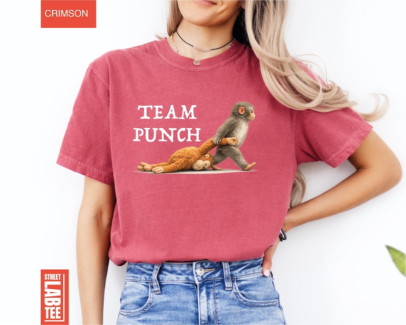 May include: Crimson red t-shirt with the text "TEAM PUNCH" in white. The shirt features a graphic of a monkey dragging a stuffed animal. The shirt is made of a soft material.
