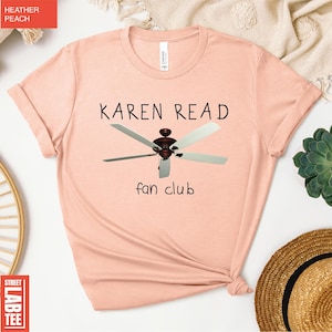 May include: A peach-colored t-shirt with the text "KAREN READ fan club" printed in black. The graphic features a ceiling fan illustration. The shirt is made of a soft material and has rolled-up sleeves.