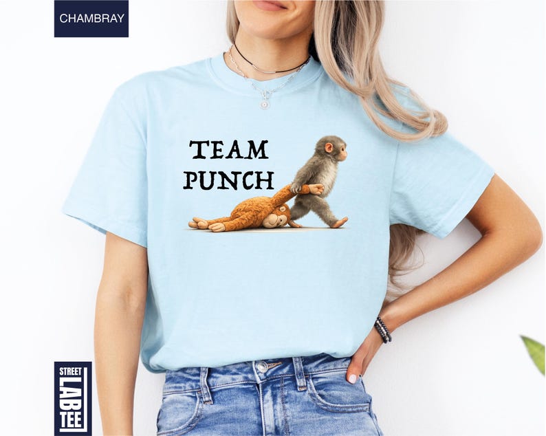 May include: Light blue t-shirt with the text "TEAM PUNCH" in black. The shirt features a cartoon illustration of two monkeys, one pulling the other. The shirt is made of a soft material.