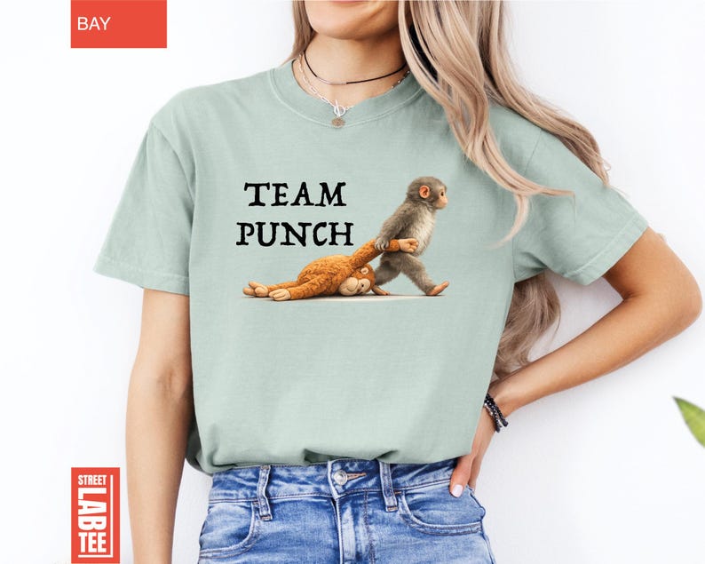 May include: A light green t-shirt with the text "TEAM PUNCH" above a cartoon image of two monkeys. One monkey is pulling the other by the arm. The shirt is a solid color.