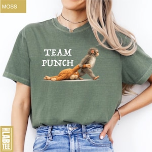 May include: Moss green t-shirt with the text "TEAM PUNCH" in white. The shirt features a cartoon illustration of a monkey pulling another monkey. The shirt is made of a soft, comfortable material.
